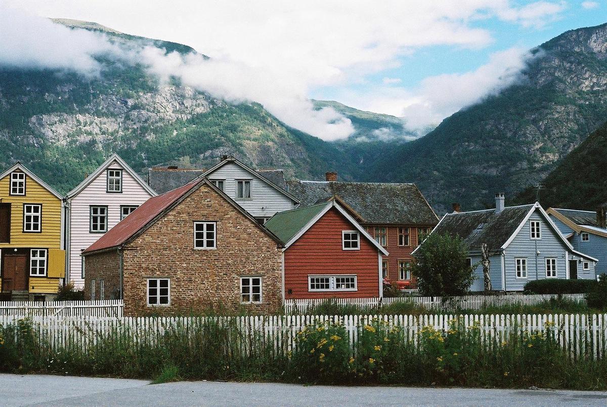 A row of houses with a white picket fence in front of a mountain range with clouds.