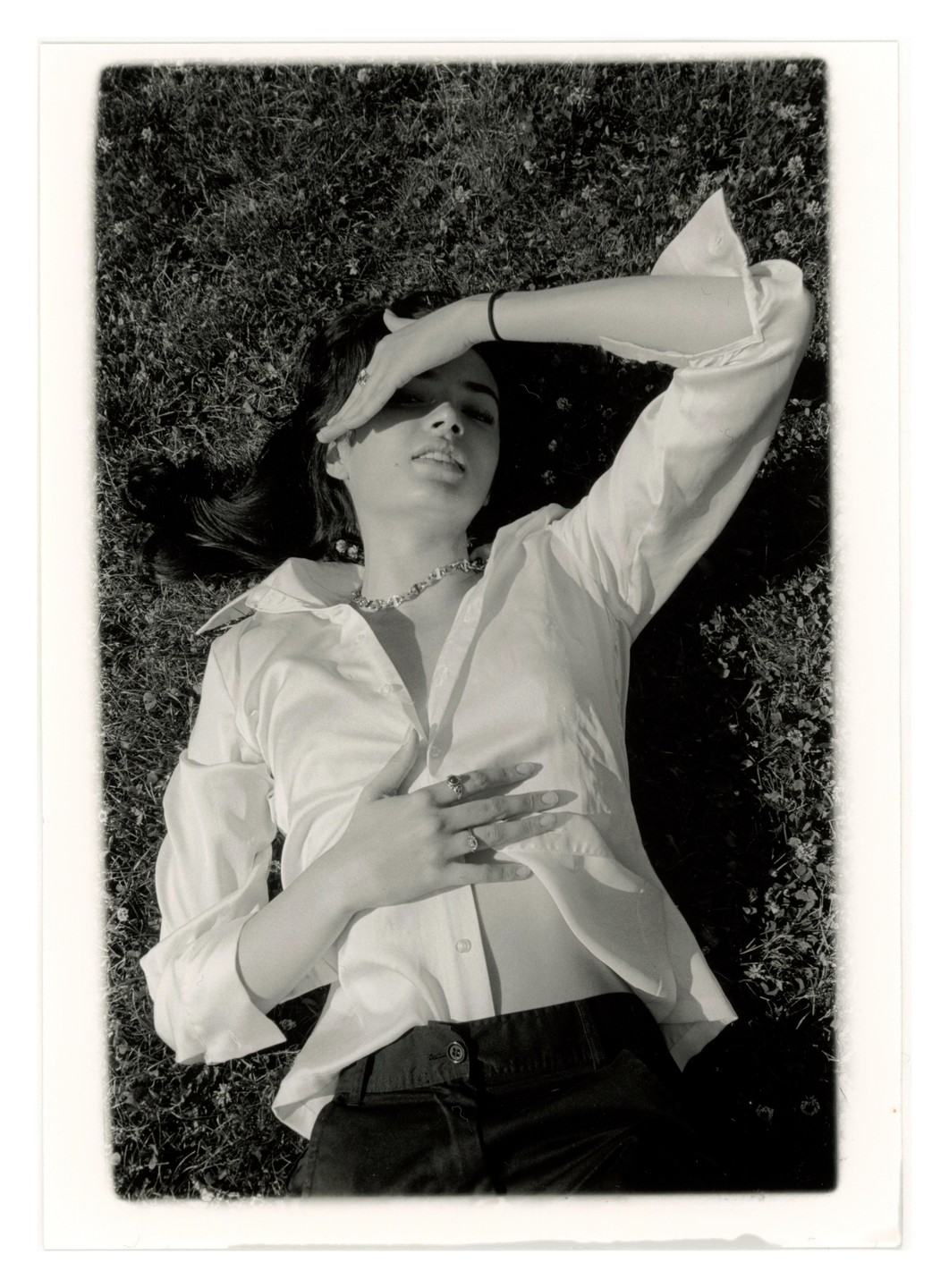 A woman lies on her back in the grass, shielding her eyes from the sun with her arm.