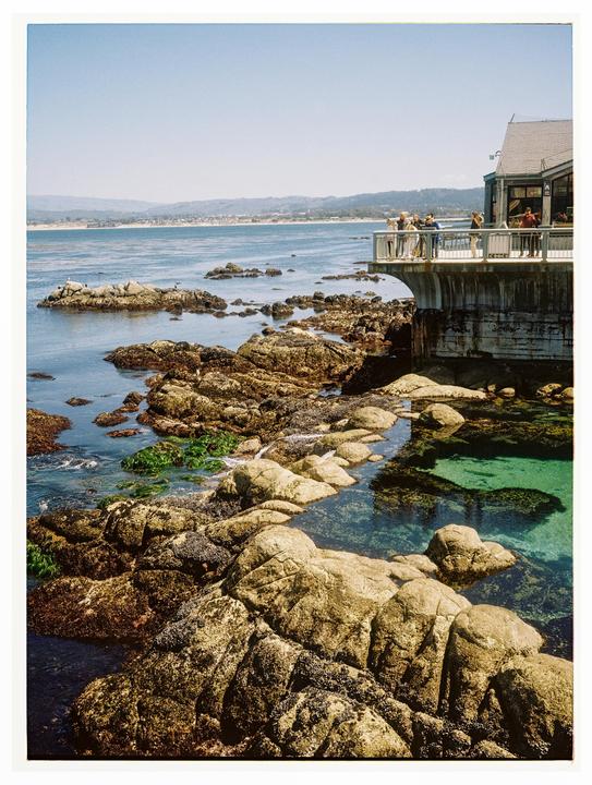 A building with a balcony overlooks a rocky coastline with tide pools and the ocean.