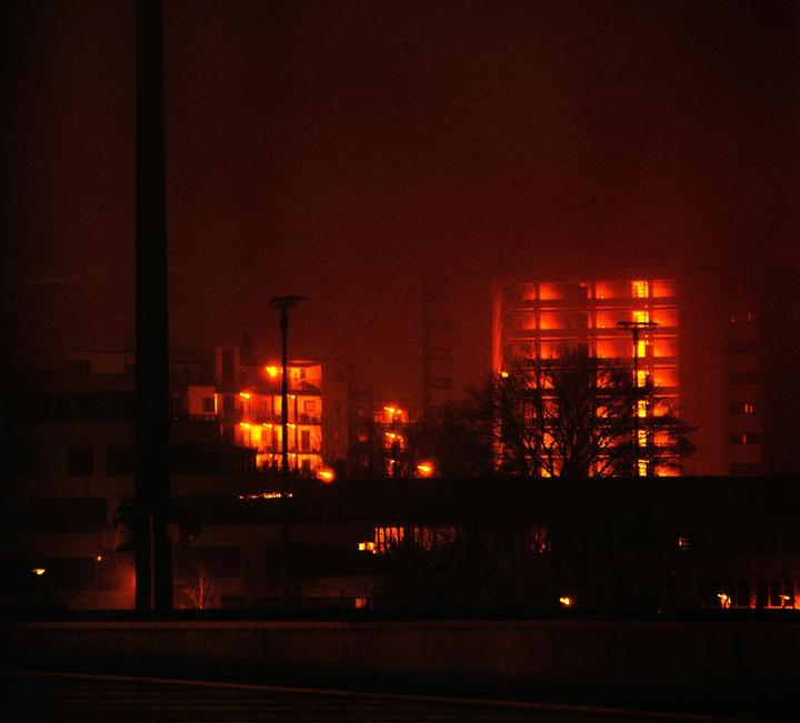 A city street is illuminated by orange lights from buildings and streetlights at night.