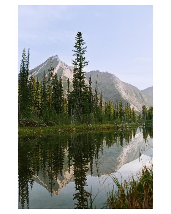 A mountain and forest are reflected in a still lake.