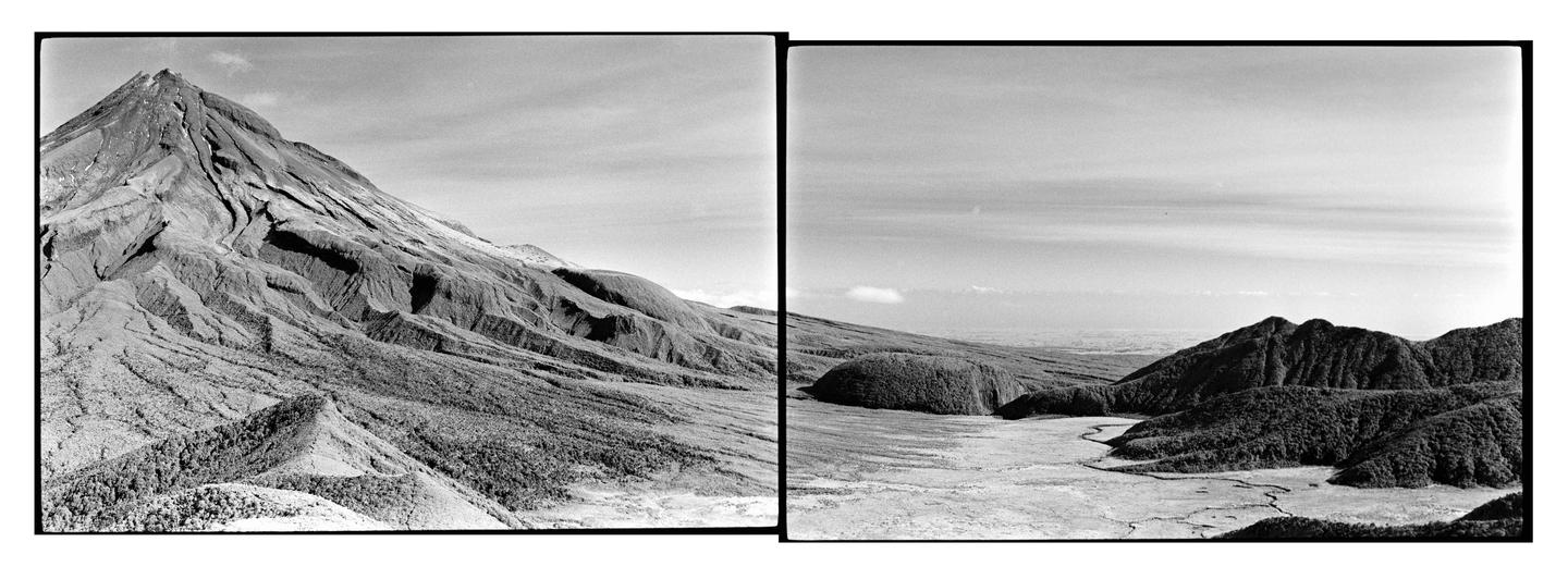 A panoramic black and white landscape shows a large mountain on the left and a valley with smaller hills and a winding river on the right.