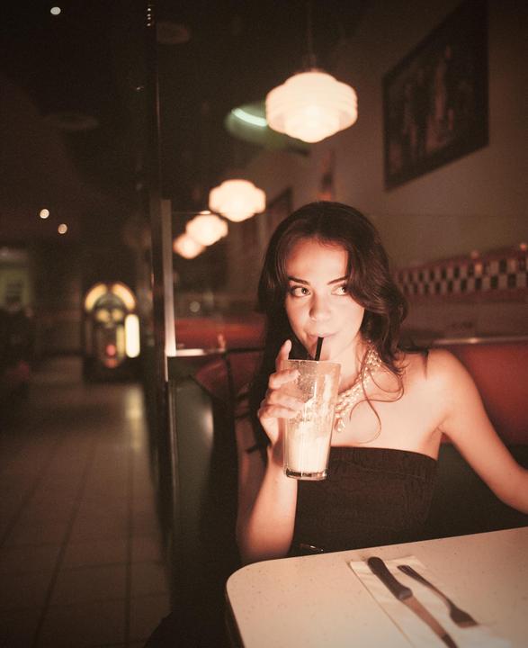 A woman sips a milkshake in a diner booth.