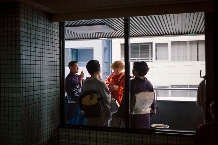 Four people are gathered on a balcony, viewed through a window from an indoor tiled area.