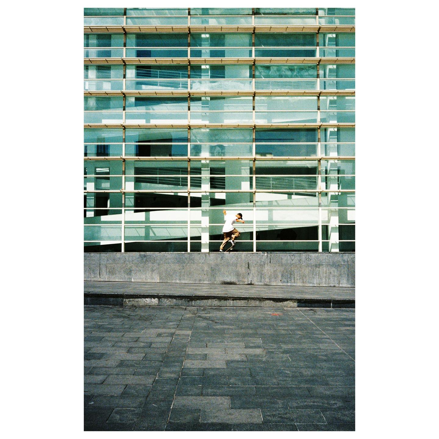 A man on a skateboard is in front of a modern building with many windows.