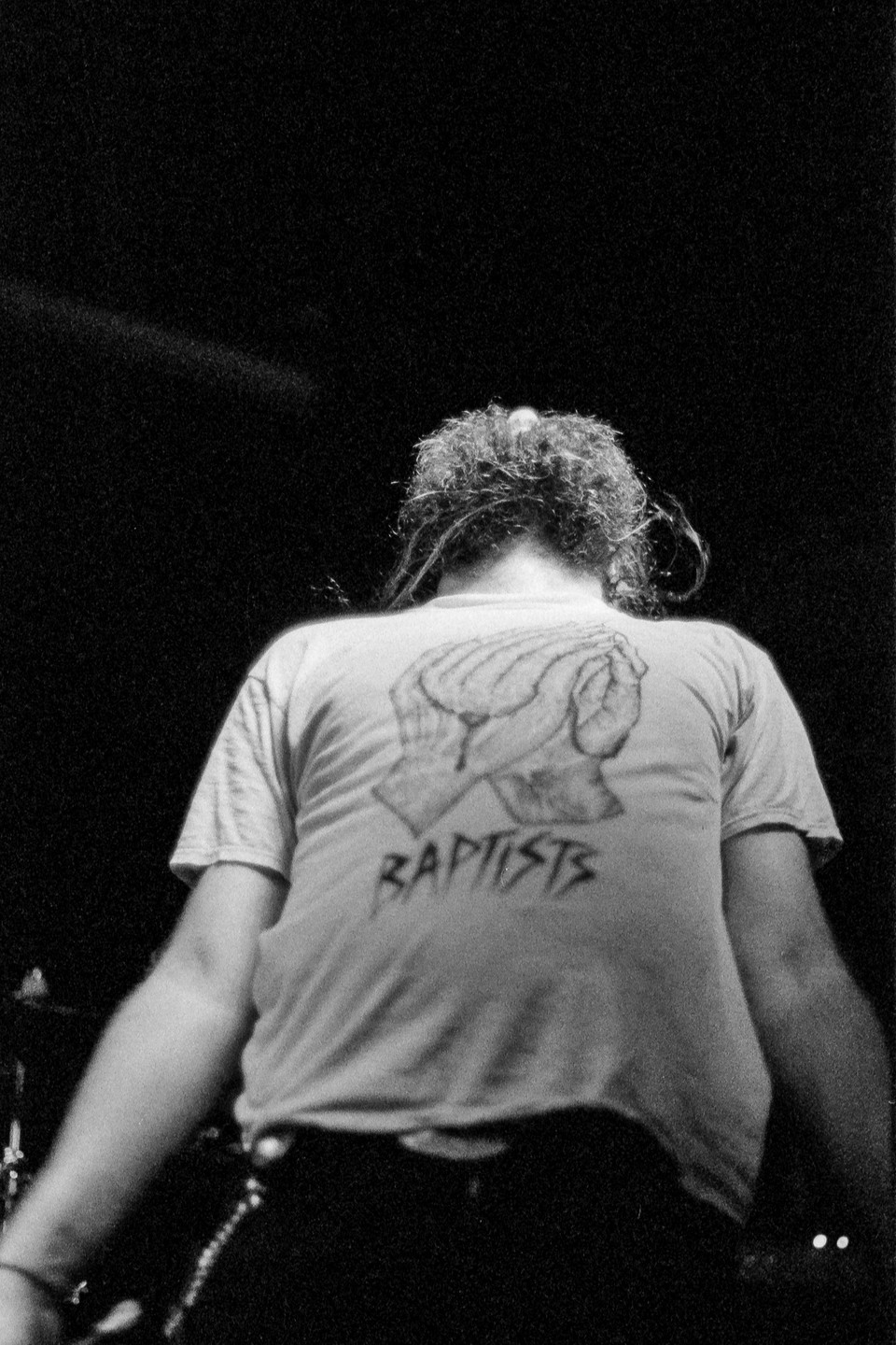 A person with curly hair is seen from behind, wearing a t-shirt with a graphic of praying hands and the word "BAPTISTS" on it.