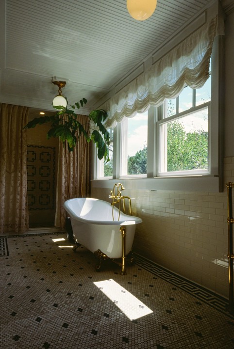 Sunlight streams into a bathroom with a clawfoot bathtub, patterned tile floor, and large windows.