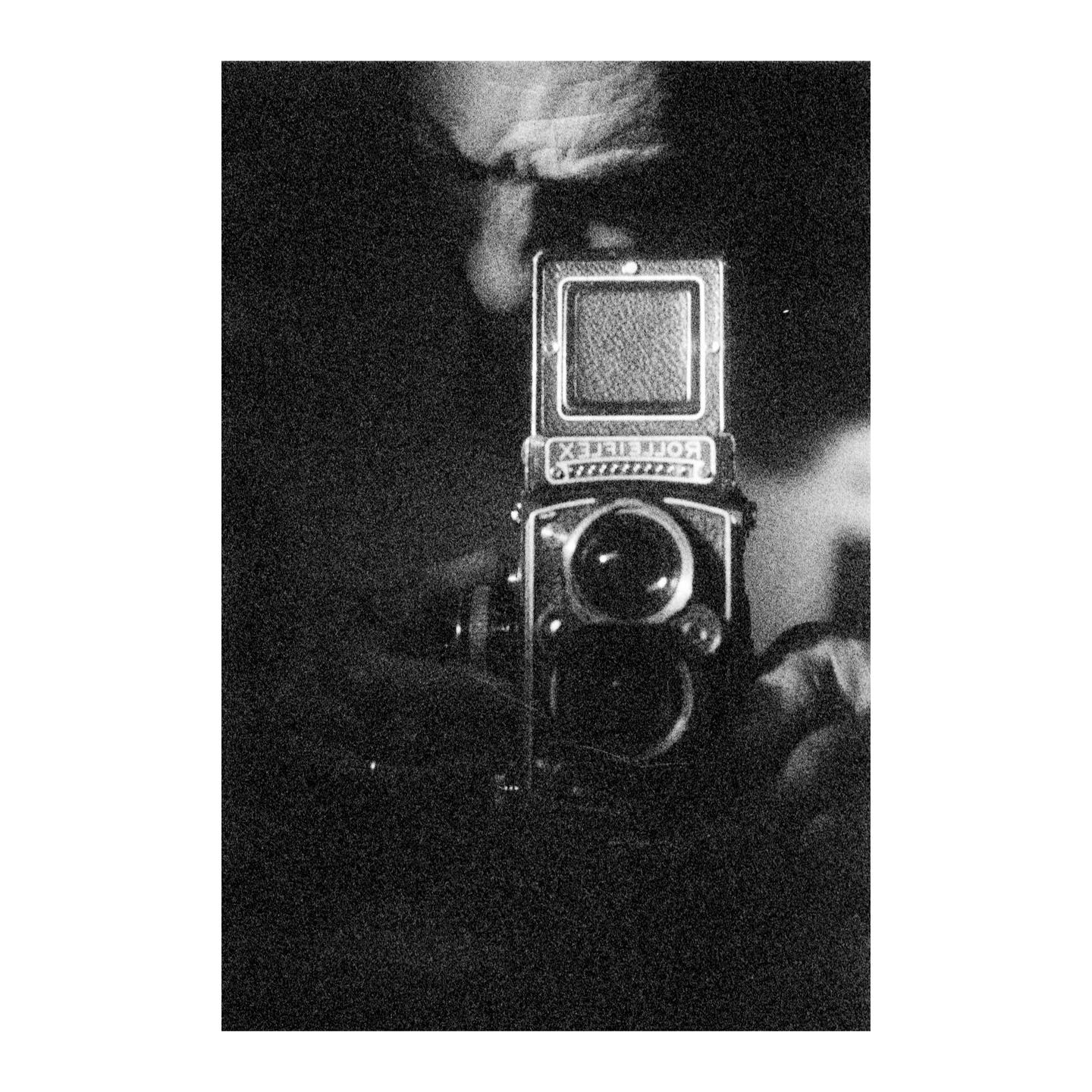 A Rolleiflex camera is held up, with its name visible in reverse.
