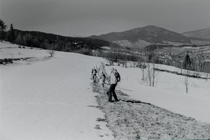 A group of people walk on a snowy path with mountains in the background.
