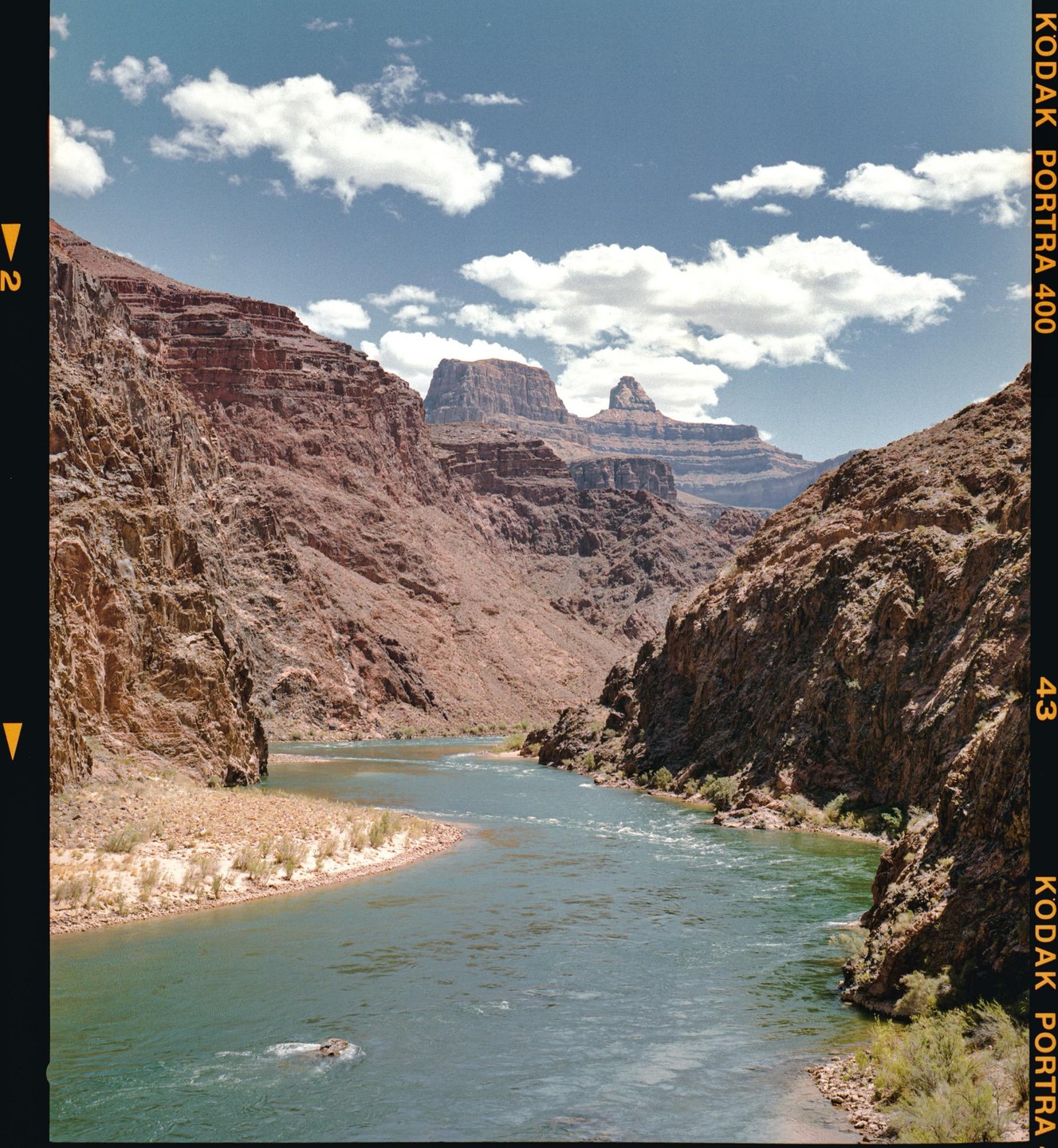 A river flows through a canyon under a blue sky with clouds.