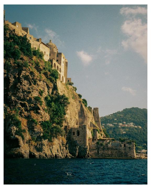 A large stone building with a domed roof is built into the side of a cliff overlooking the sea.