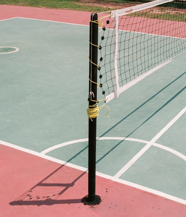 A volleyball net stands on a court with red and green sections and white lines.