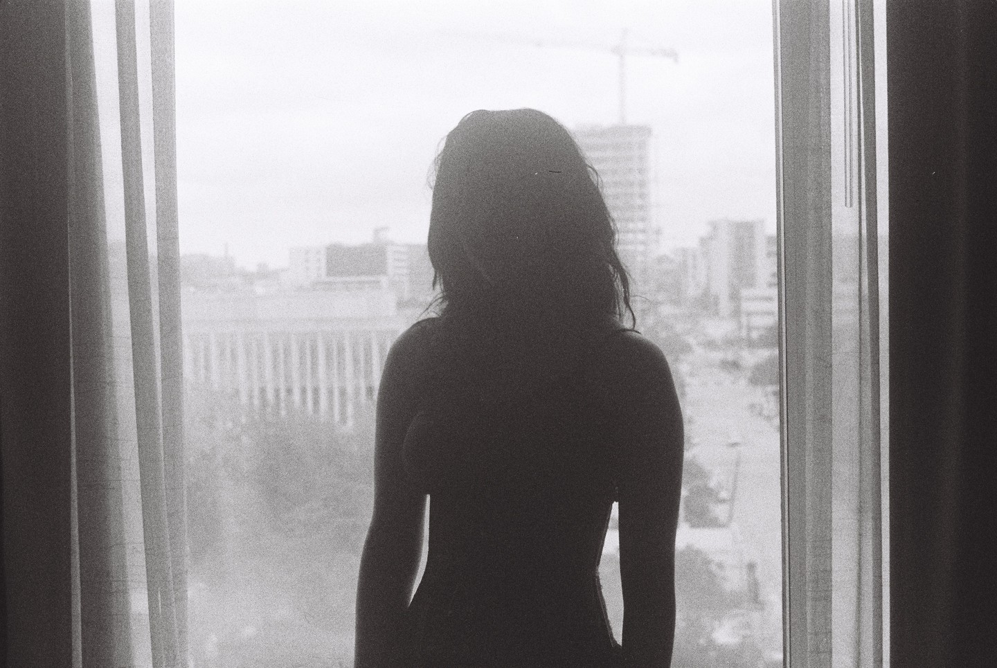 A woman stands silhouetted against a window overlooking a city.