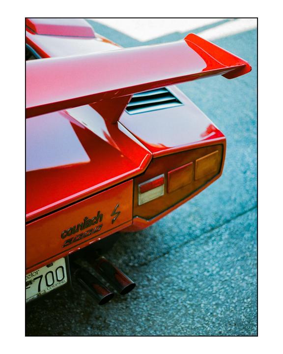 A red sports car with a large spoiler is parked on an asphalt surface.