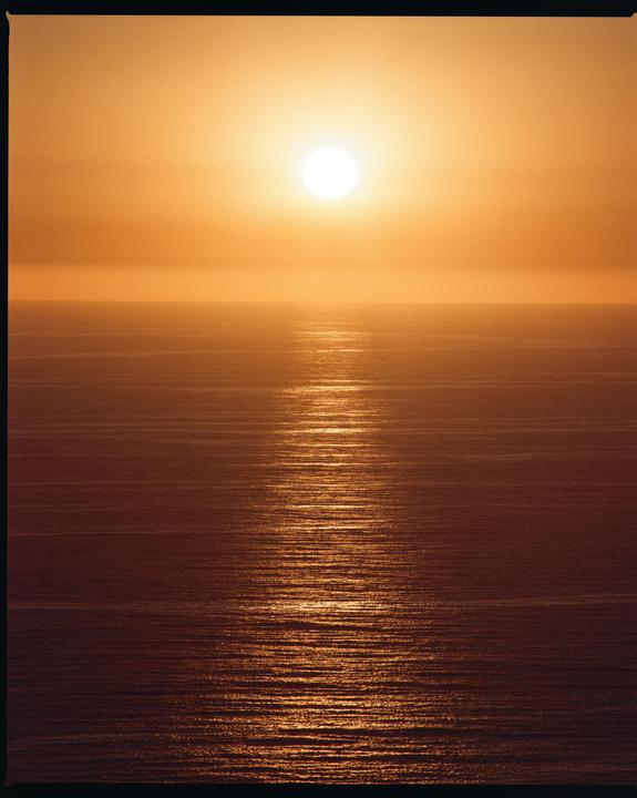 The sun sets over the ocean, creating a bright reflection on the water.