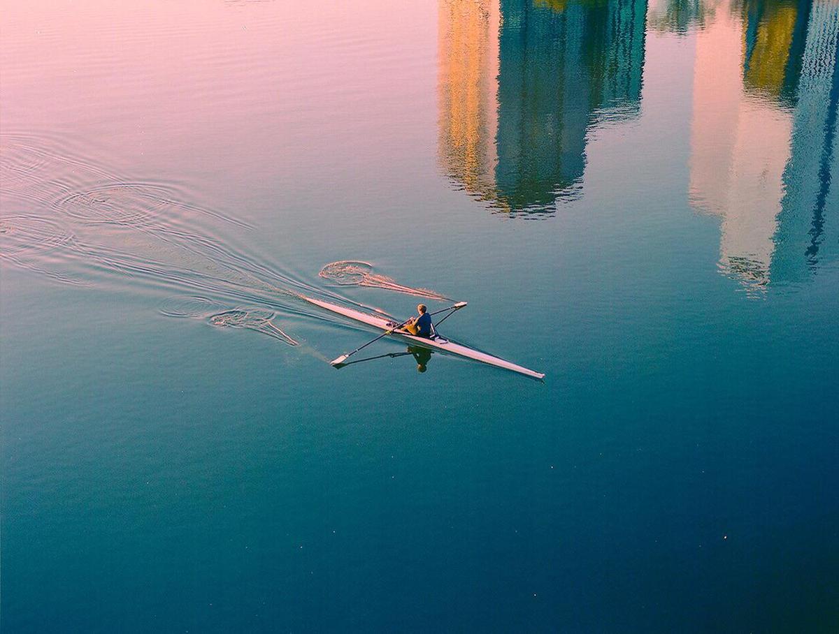 A person rows a boat on a body of water with reflections of buildings.