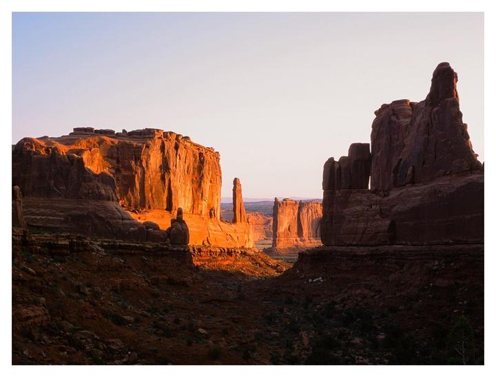 A desert landscape features large rock formations illuminated by the rising sun.