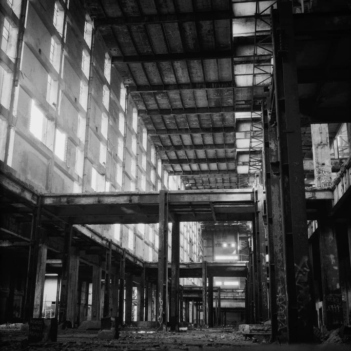 The interior of an abandoned power station shows multiple levels of concrete and steel structures with many windows on the left wall.