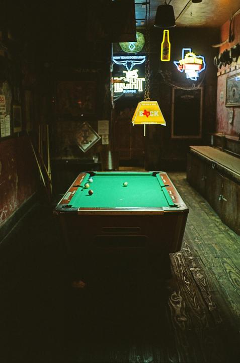 A pool table with several balls on it sits in a dimly lit room with neon signs on the wall.