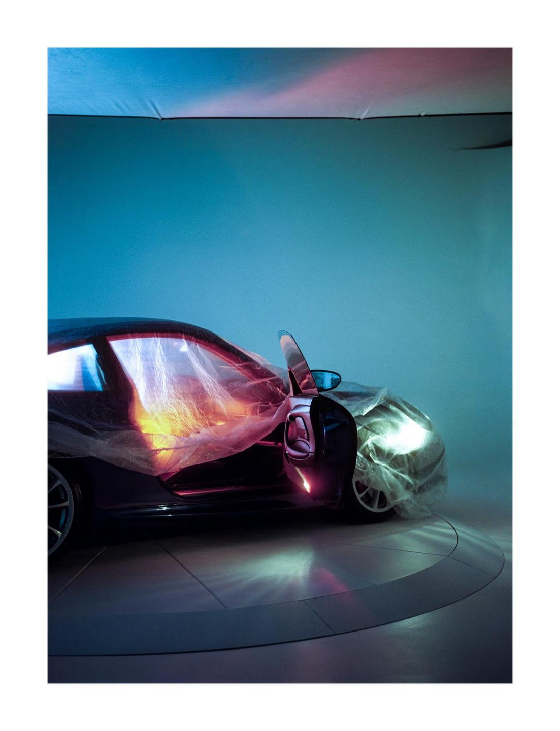 A car is covered with plastic sheeting in a studio with colorful lighting.