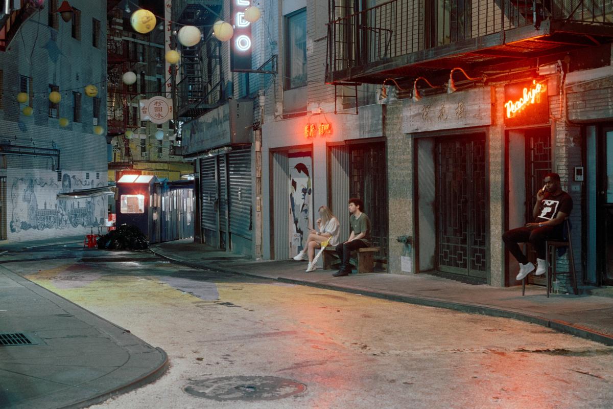 Three people are sitting on a street at night in Chinatown.
