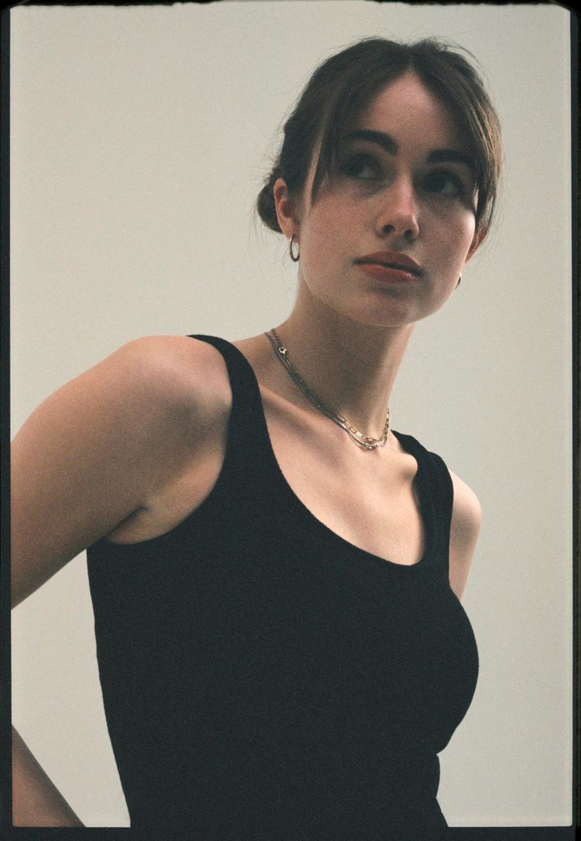 A young woman with her hair pulled back and bangs framing her face looks up and to the right.