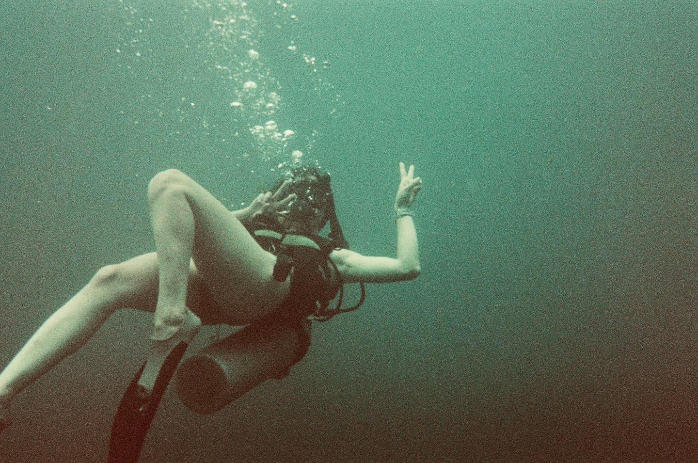 A woman scuba diver floats underwater, making a peace sign with both hands.