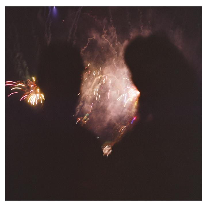 Two silhouettes of people are visible against a backdrop of colorful fireworks exploding in the night sky.