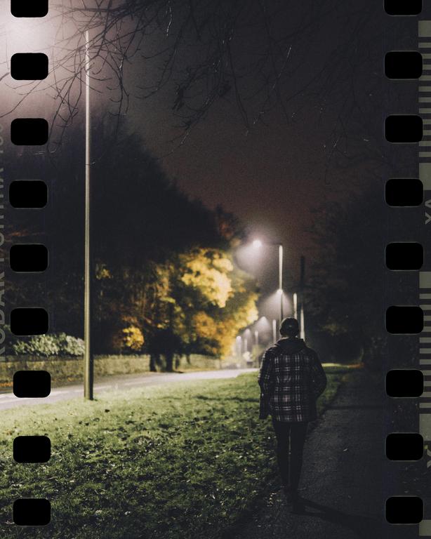 A person walks along a path at night, illuminated by streetlights.