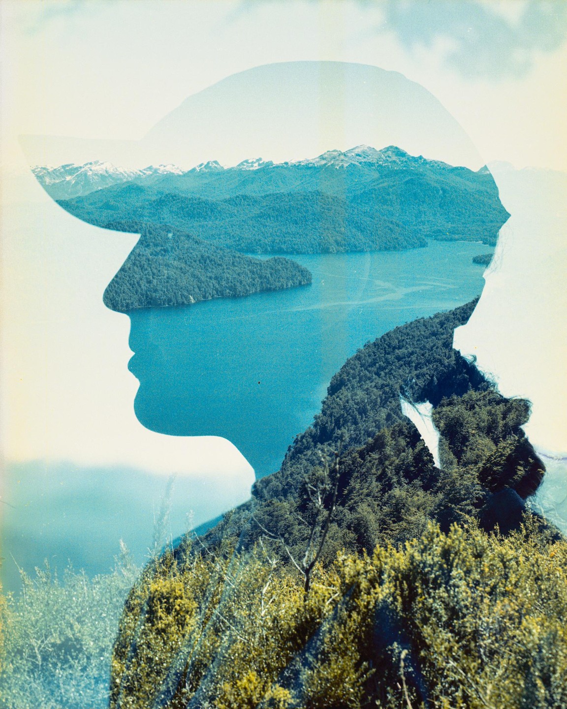 A double exposure shows a profile of a person wearing a hat superimposed over a landscape of a lake, forest, and mountains.