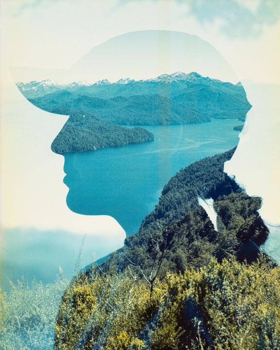 A double exposure shows a profile of a person wearing a hat superimposed over a landscape of a lake, forest, and mountains.