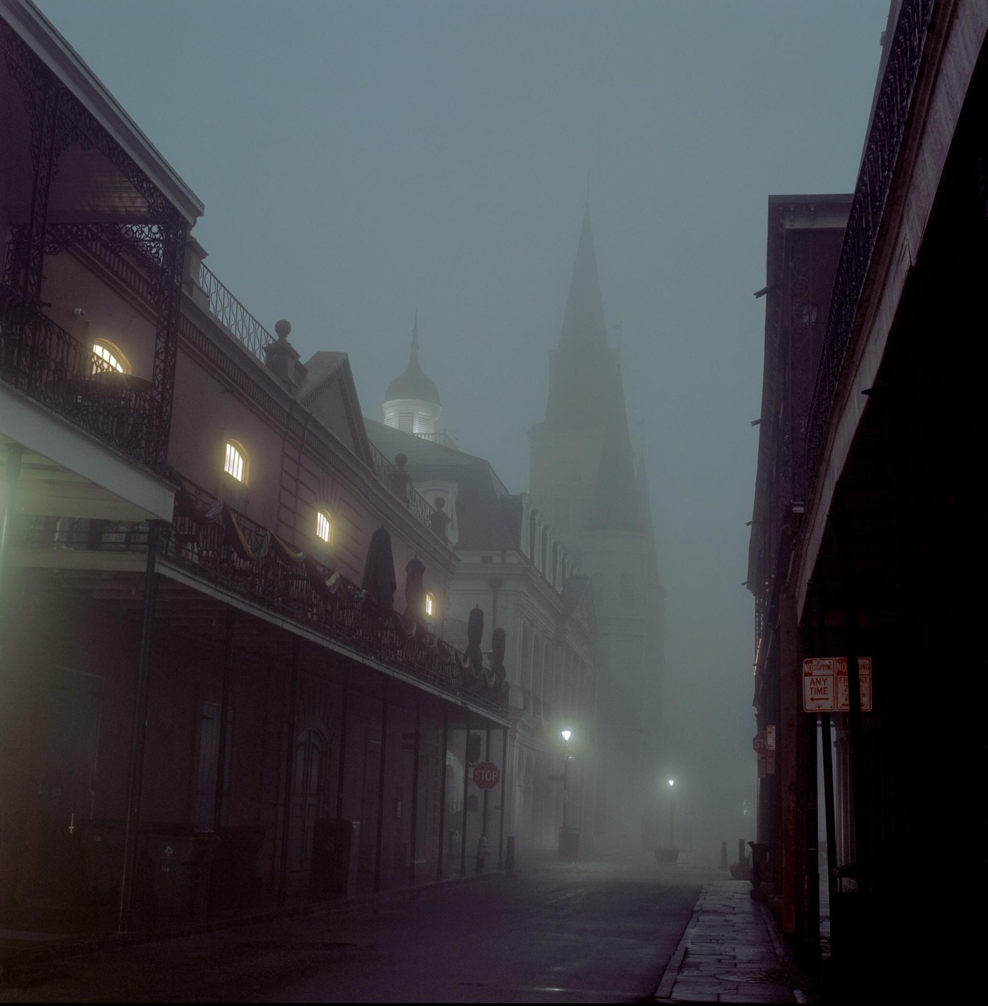 A street with buildings and a church steeple is shrouded in fog at twilight.