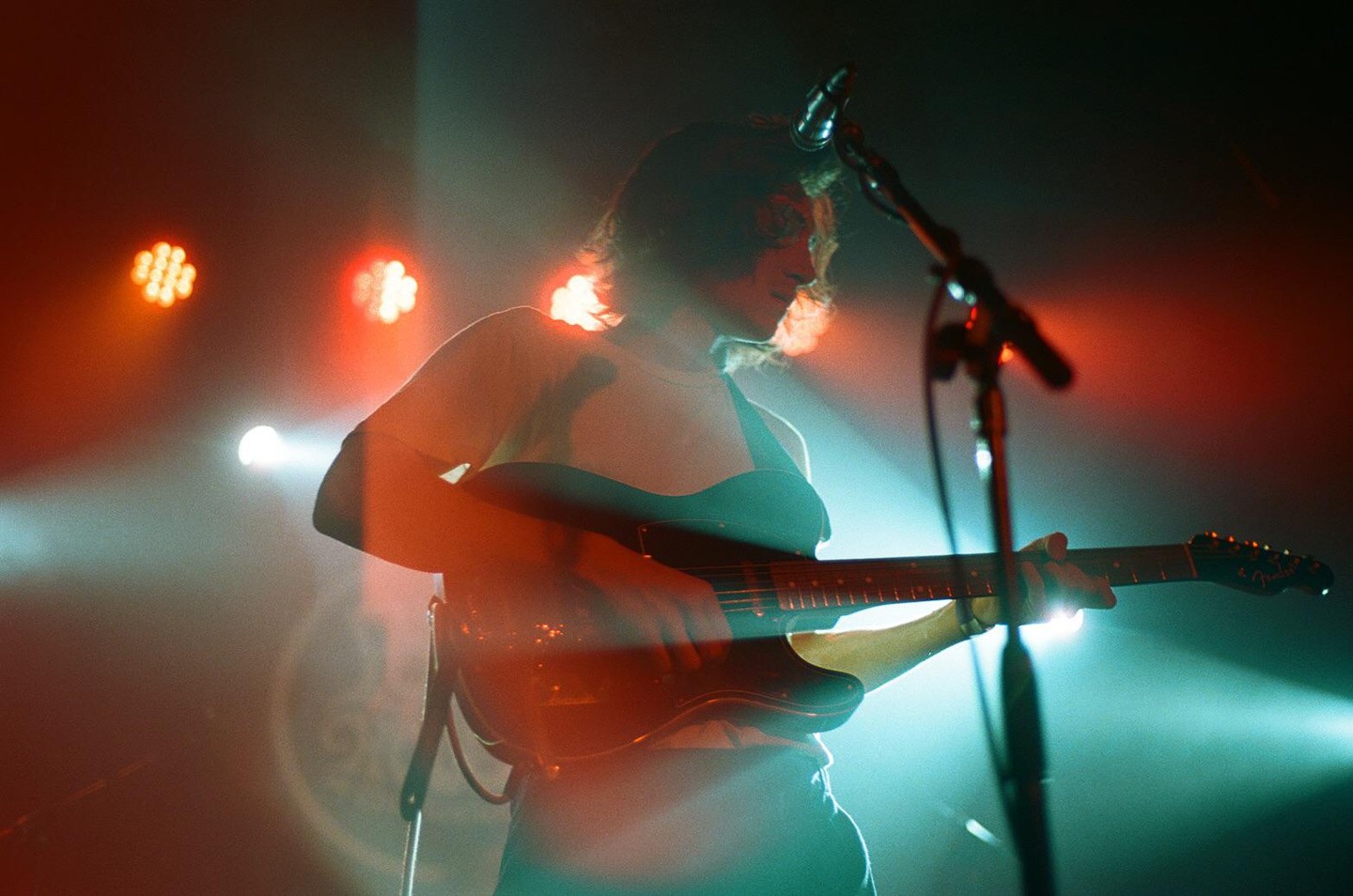 A musician plays an electric guitar on a stage lit by red and blue lights.