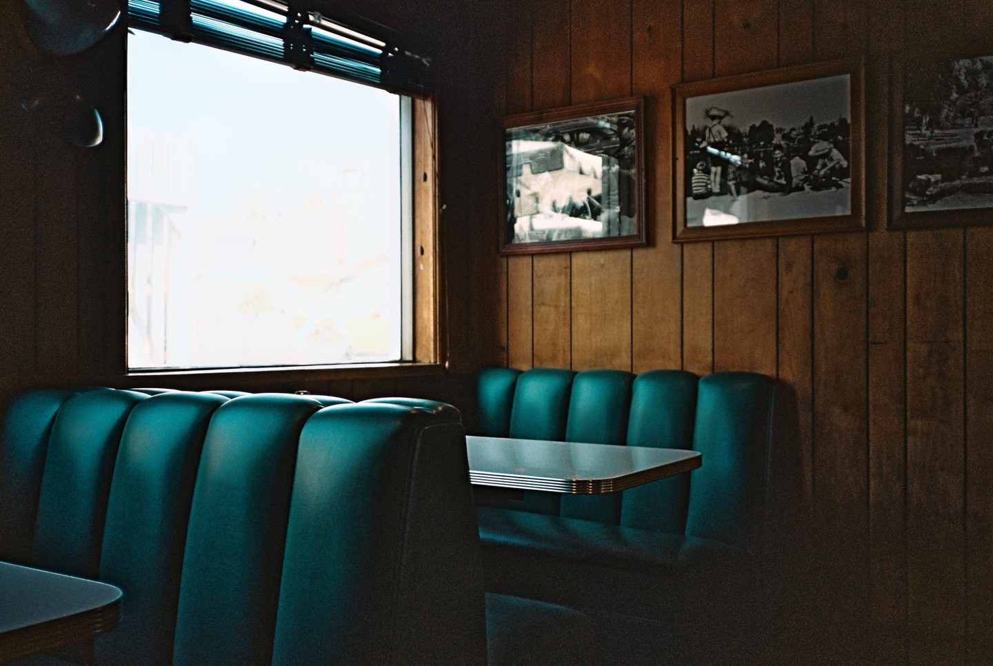 A diner booth with teal upholstery and a window is shown from a low angle.