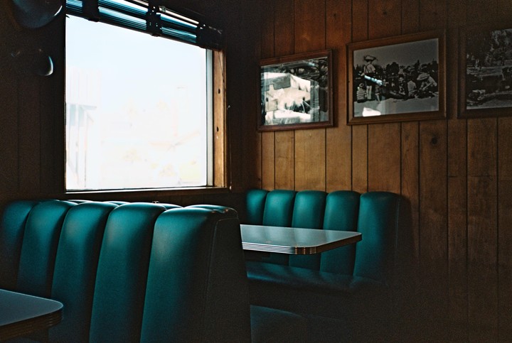 A diner booth with teal upholstery and a window is shown from a low angle.
