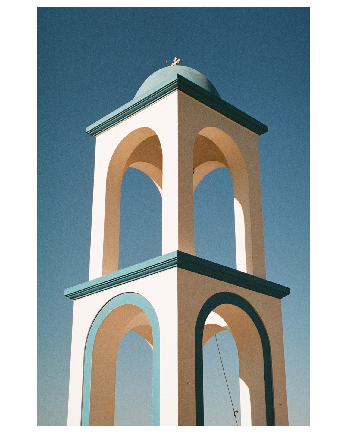A white church bell tower with a teal dome and cross stands against a clear blue sky.