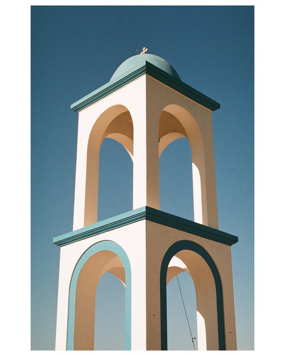 A white church bell tower with a teal dome and cross stands against a clear blue sky.