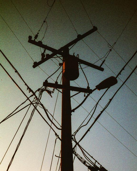 A utility pole with many wires and a street light is silhouetted against the sky.