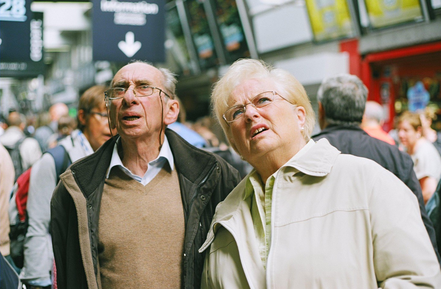 A man and a woman look up with confused expressions in a crowded indoor setting.