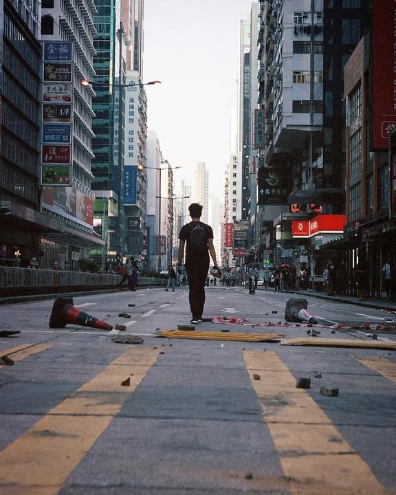 A man walks down a street littered with debris and traffic cones, surrounded by tall buildings with signs.