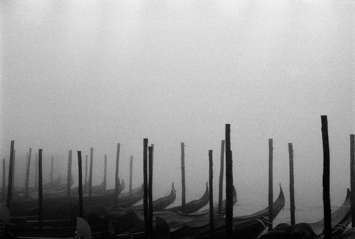 Gondolas are moored in a foggy canal in Venice.
