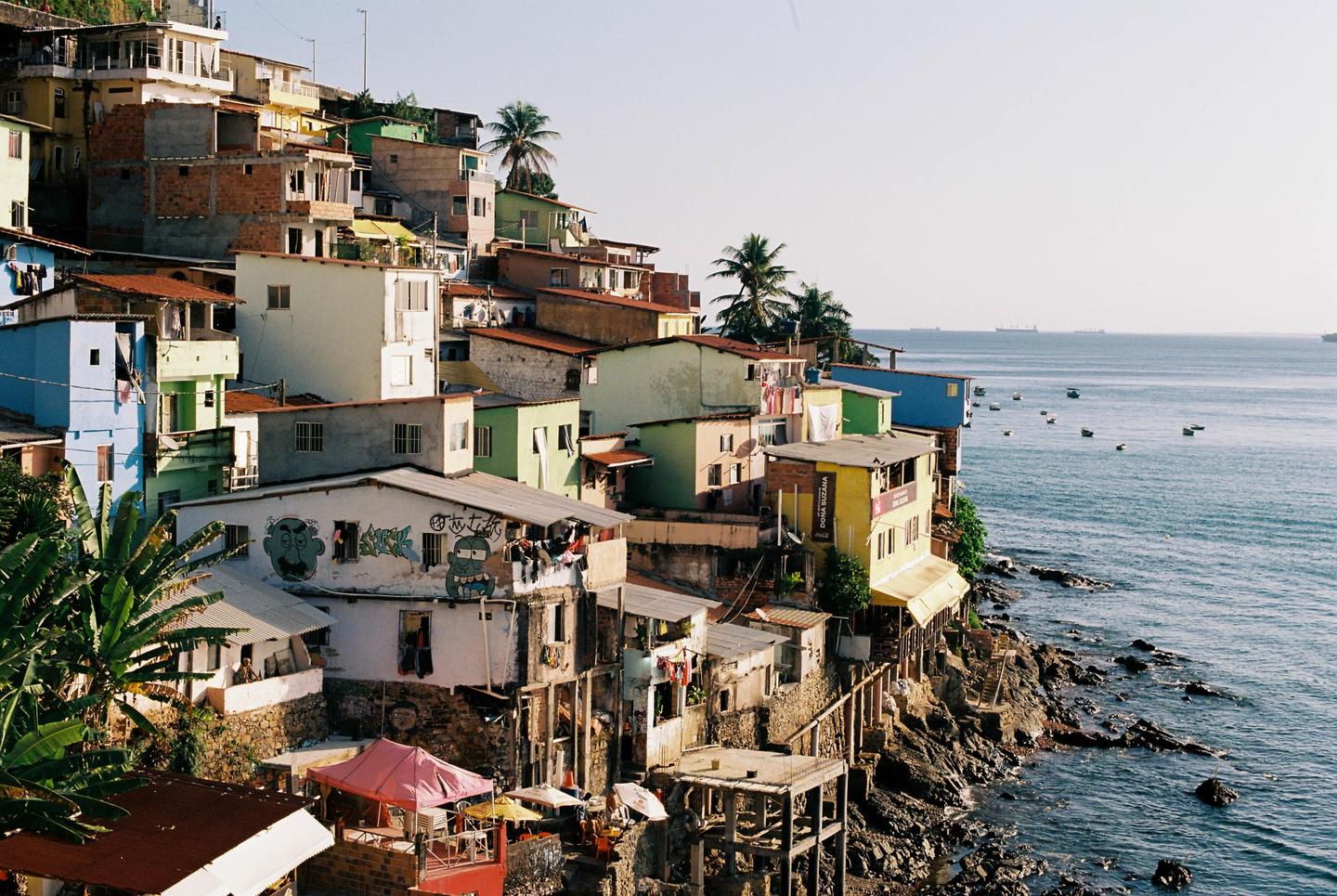 A hillside favela with colorful houses overlooks a bay with boats and ships.