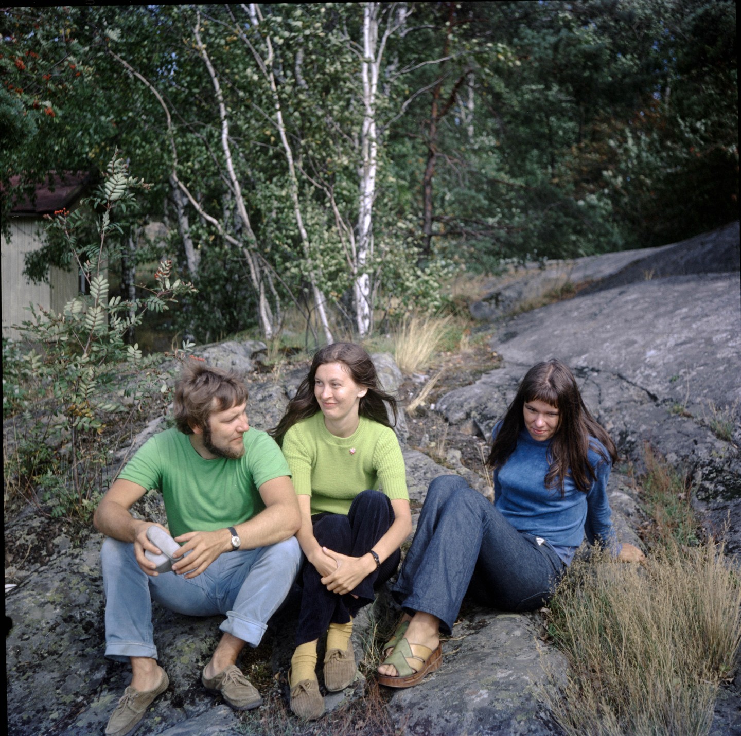 A man and two women sit on rocks in a forest.
