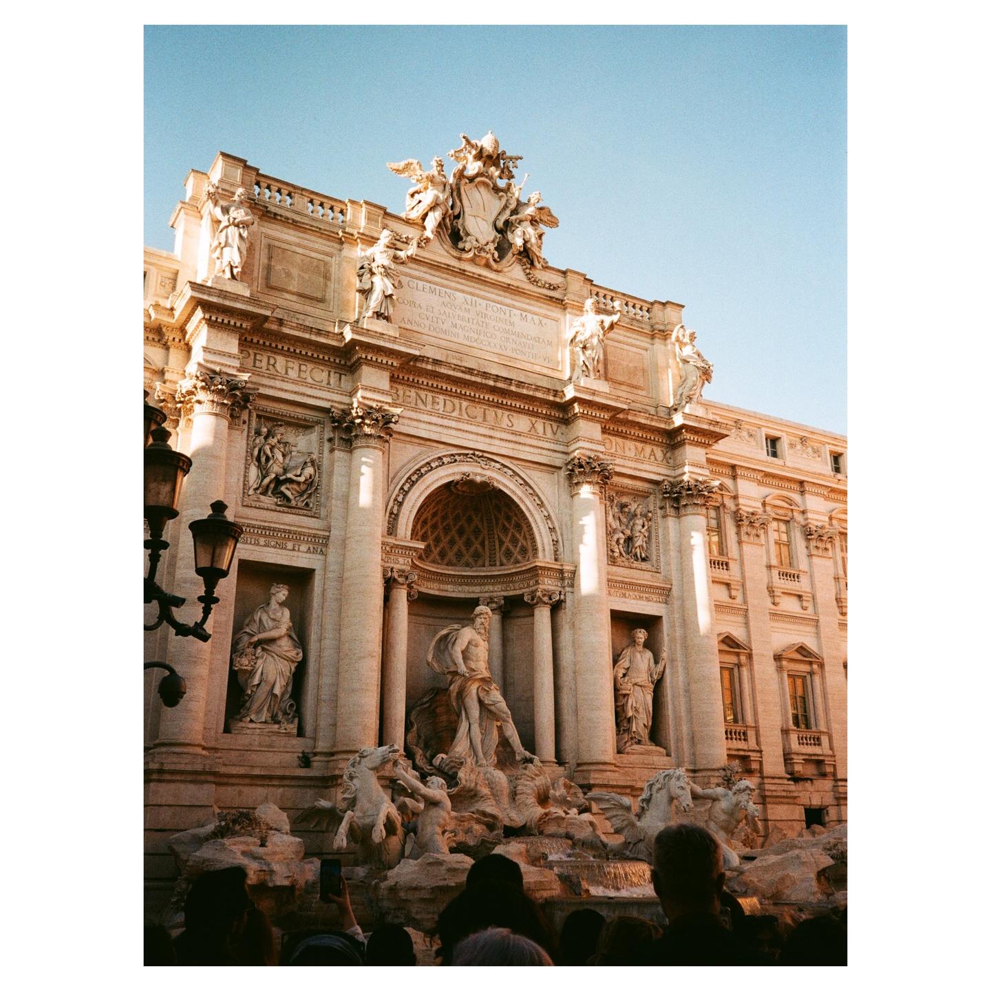 The Trevi Fountain is shown from a low angle, with a crowd of people visible at the bottom of the frame.