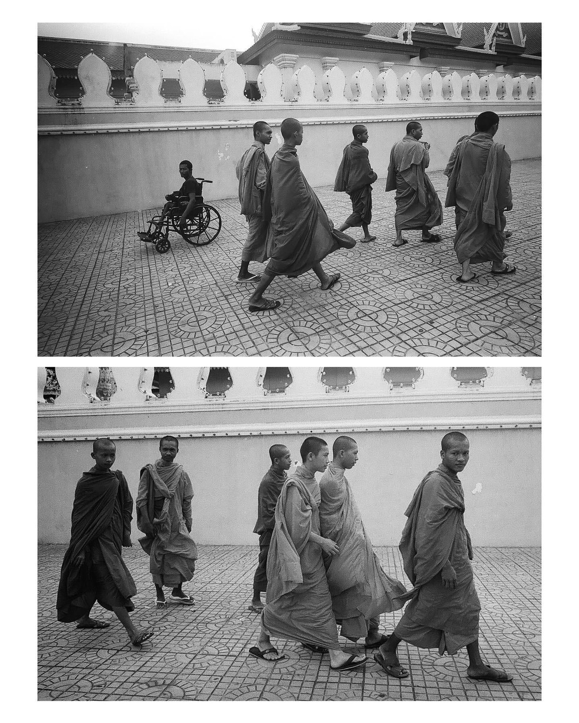 A group of monks walk on a patterned ground next to a white wall, with one monk in a wheelchair in the background.