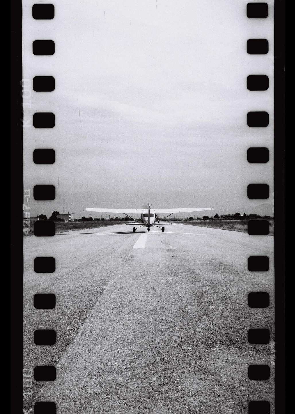 A small airplane is seen from behind on a runway with film borders on the sides.