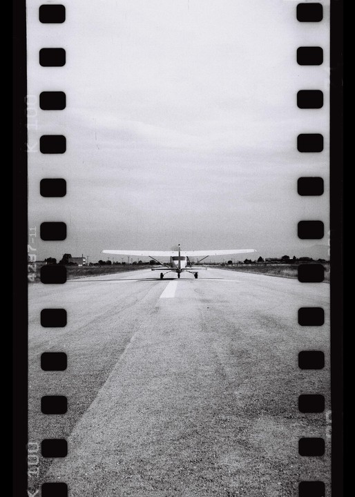 A small airplane is seen from behind on a runway with film borders on the sides.