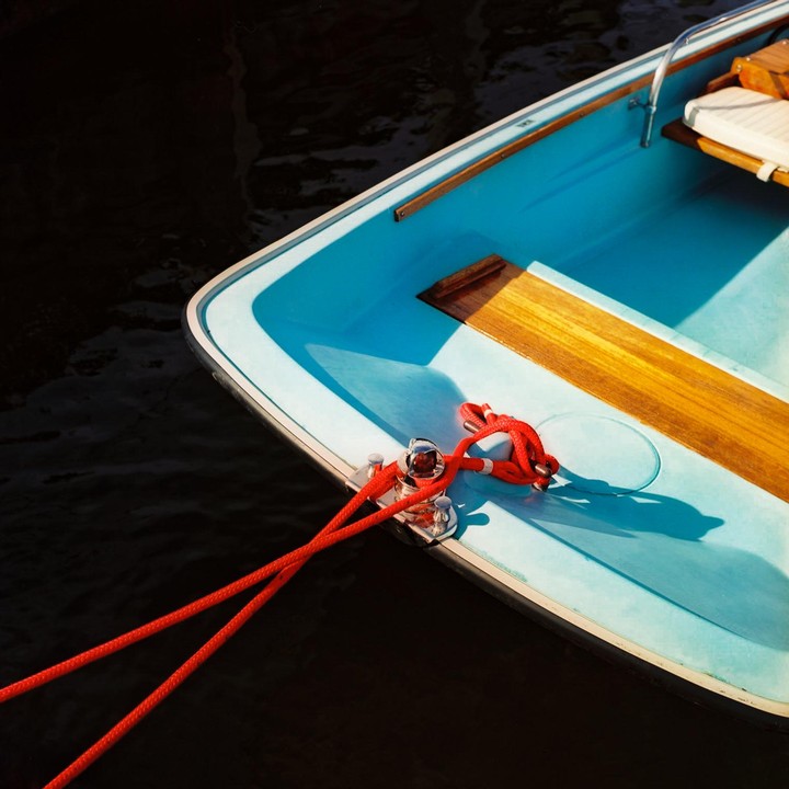 A blue boat with red ropes is tied to a dock.