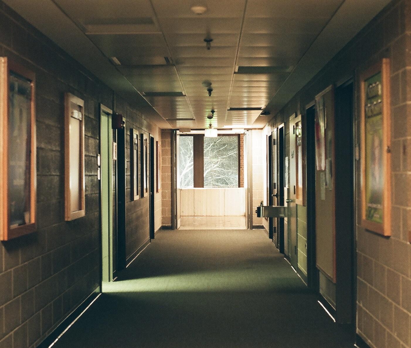 A long, empty hallway with a window at the end looks out onto snow-covered tree branches.