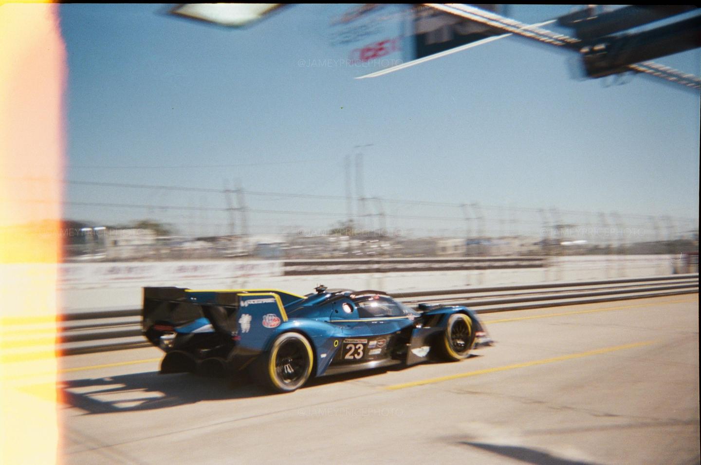 A blue race car with the number 23 is speeding on a track under a clear sky.